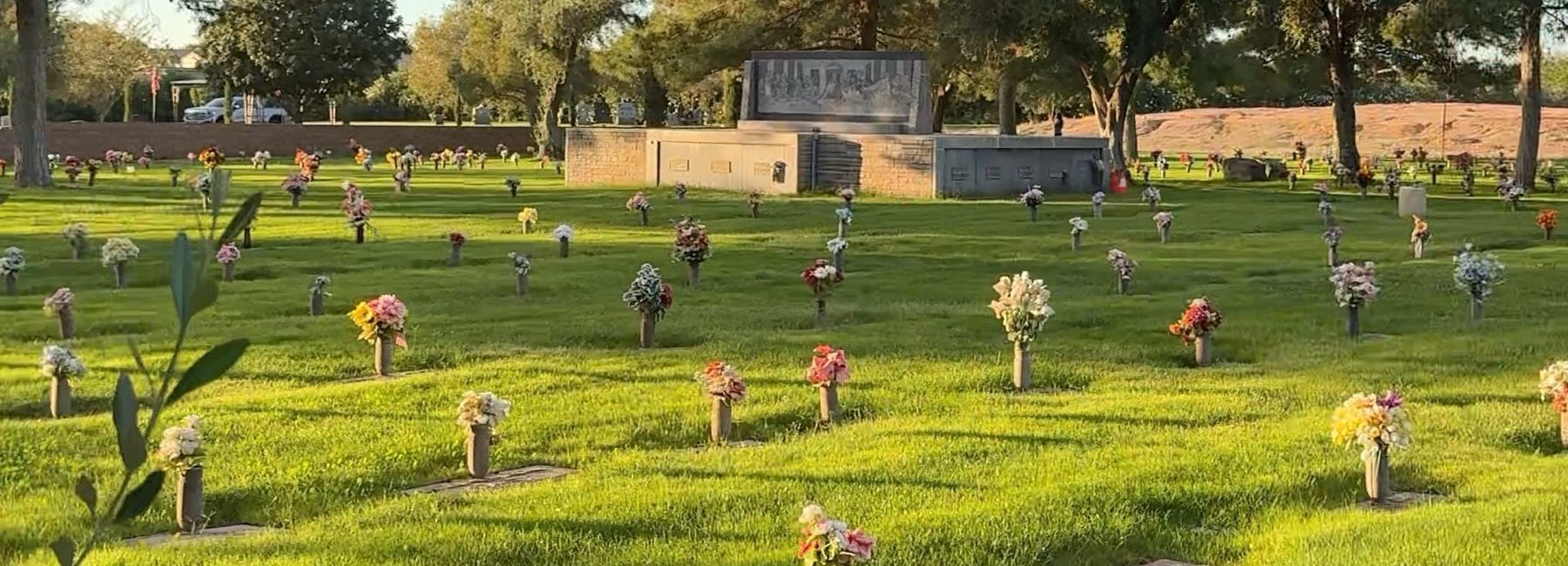A lawn section at Mountain View Cemetery in late afternoon light, flowers standing at the markers